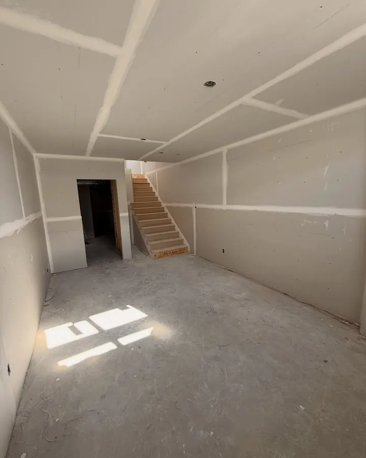 A basement with every seam and corner taped and mudded, stairs at the back.